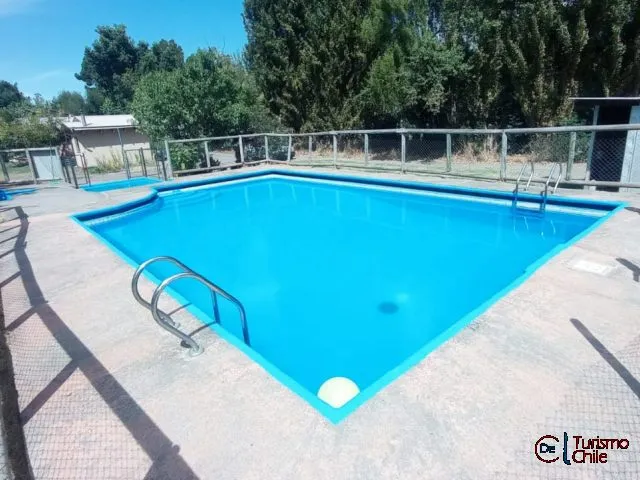 Piscina azul exterior con escalera metálica y árboles al fondo