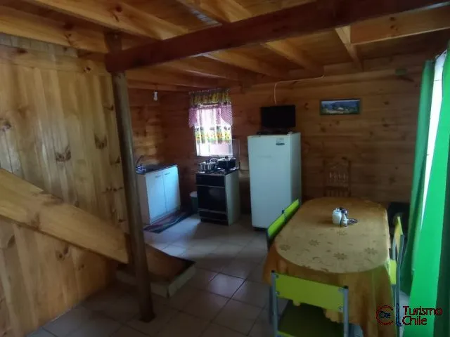 Interior de cabaña de madera con cocina, comedor y frigorífico