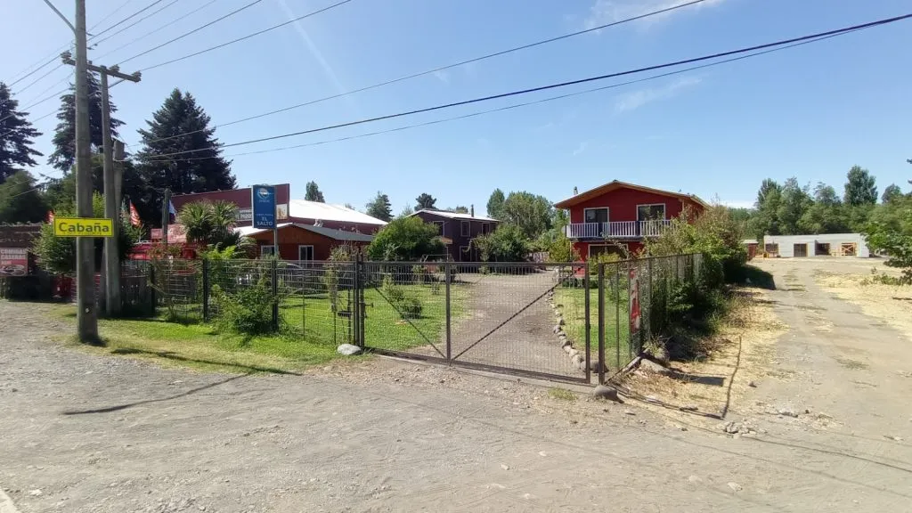 Entrada principal de Cabañas La Ita con portón y cabañas rojas en Salto del Laja