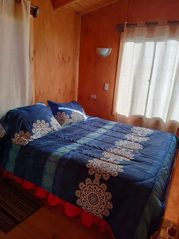Dormitorio principal con cama matrimonial y ropa de cama azul en Cabañas La Ita