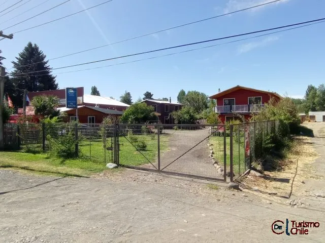 Vista frontal del acceso a Cabañas La Ita con portón de reja y cabañas rojas