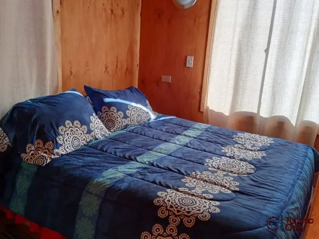 Dormitorio matrimonial con edredón azul decorado y ventana con cortinas