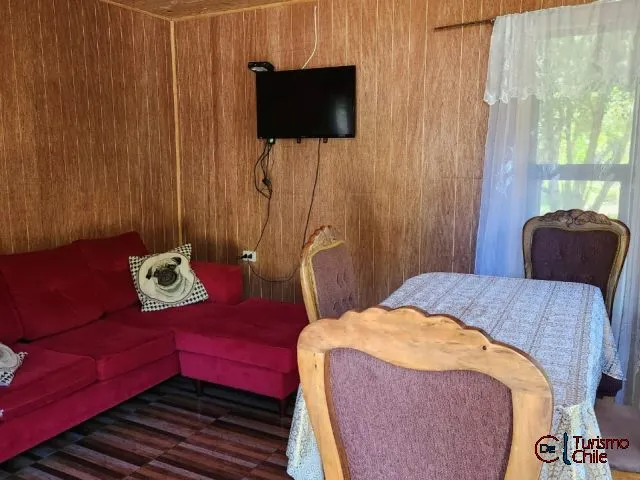 Living-comedor con sofá rojo, televisor y mesa en cabaña de madera