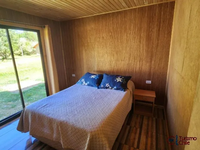 Dormitorio con cama matrimonial y paredes de madera en cabaña Las Violetas