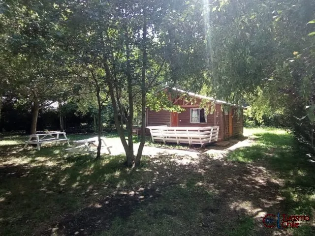 Cabaña de madera roja rodeada de árboles con terraza y bancas blancas